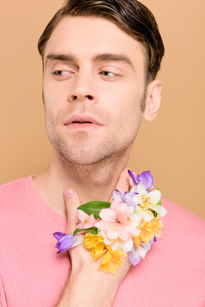 homem de mãos dadas com flores perto do pescoço isolado em bege
 - Foto, Imagem