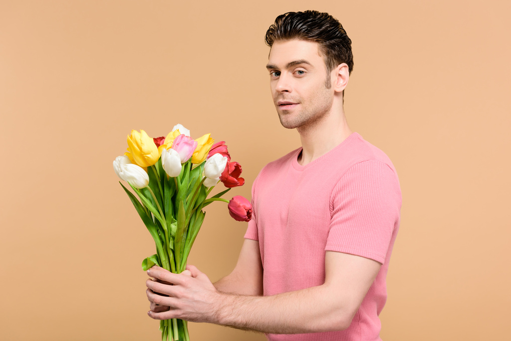 Красивый мужчина держит букет цветов, изолированных на бежевый
 - Фото, изображение