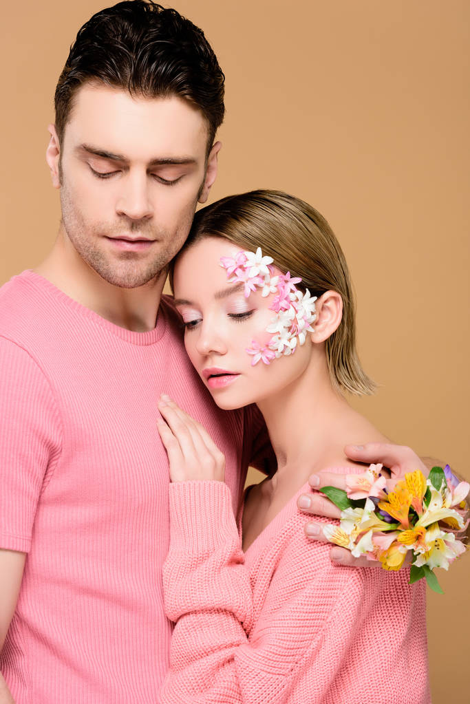 knappe man omhelst meisje met bloemen op gezicht geïsoleerd op beige  - Foto, afbeelding