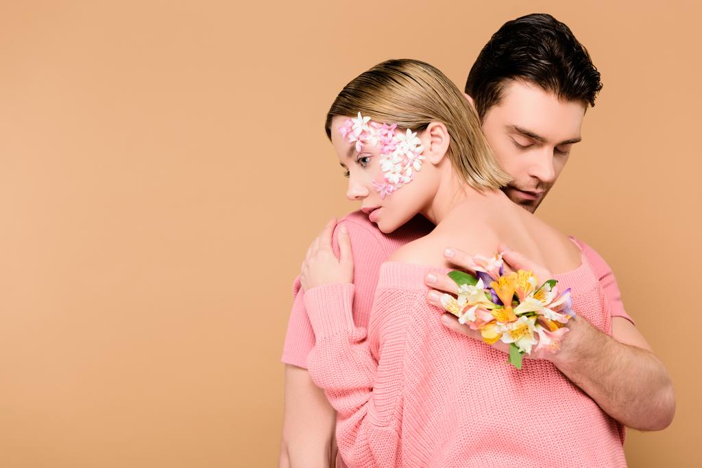 hombre con los ojos cerrados abrazando mujer con flores en la cara aislado en beige
  - Foto, Imagen