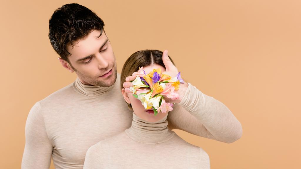 tierno hombre con flores de alstroemeria en la mano cubriendo la cara de novia aislada en beige
  - Foto, Imagen