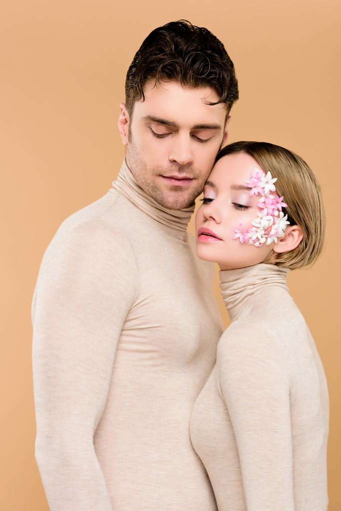 hombre guapo de pie con novia bonita con flores en la cara aislado en beige
  - Foto, imagen