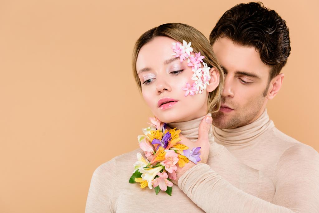 tender man with alstroemeria flowers on hand touching face of pretty woman isolated on beige  - Photo, Image