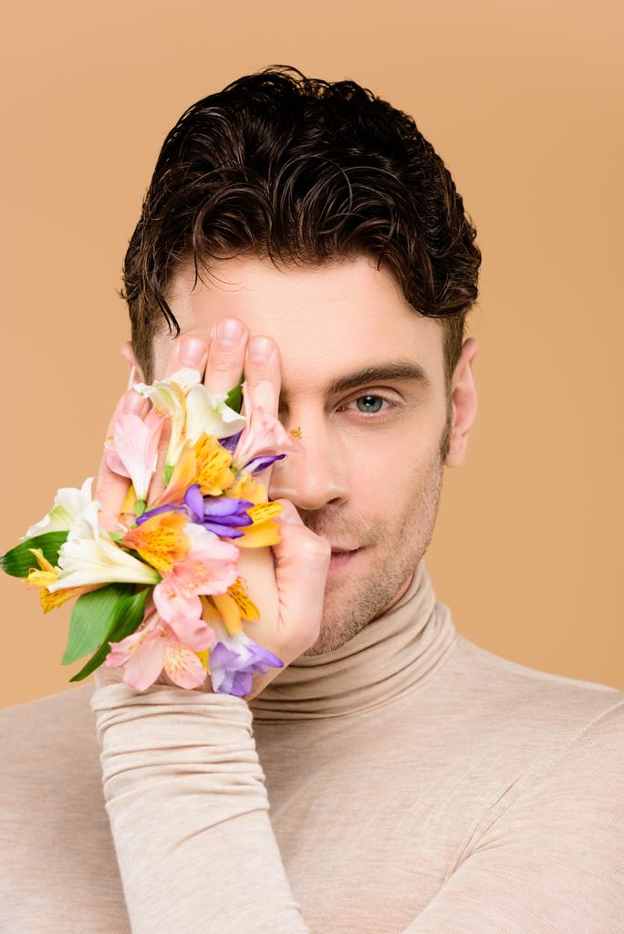 man with alstroemeria flowers on hand covering one eye isolated on beige  - Photo, Image
