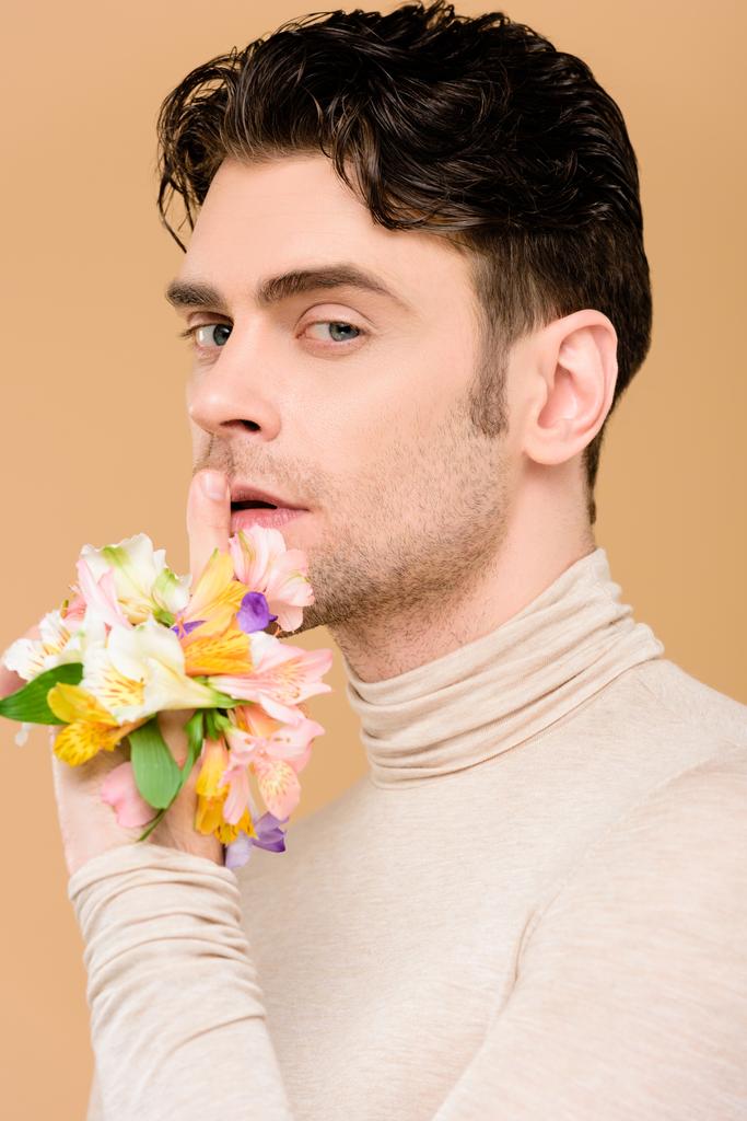  schöner Mann mit Blumen an der Hand zeigt Schweigezeichen isoliert auf beige  - Foto, Bild