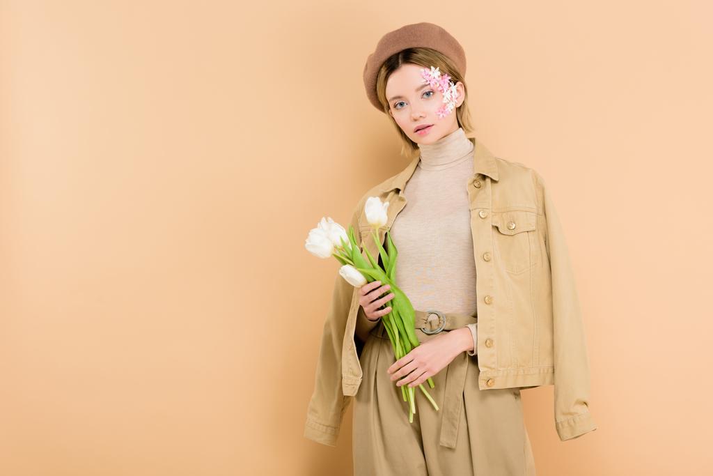 attractive woman wearing beret and holding bouquet isolated on beige  - Photo, Image