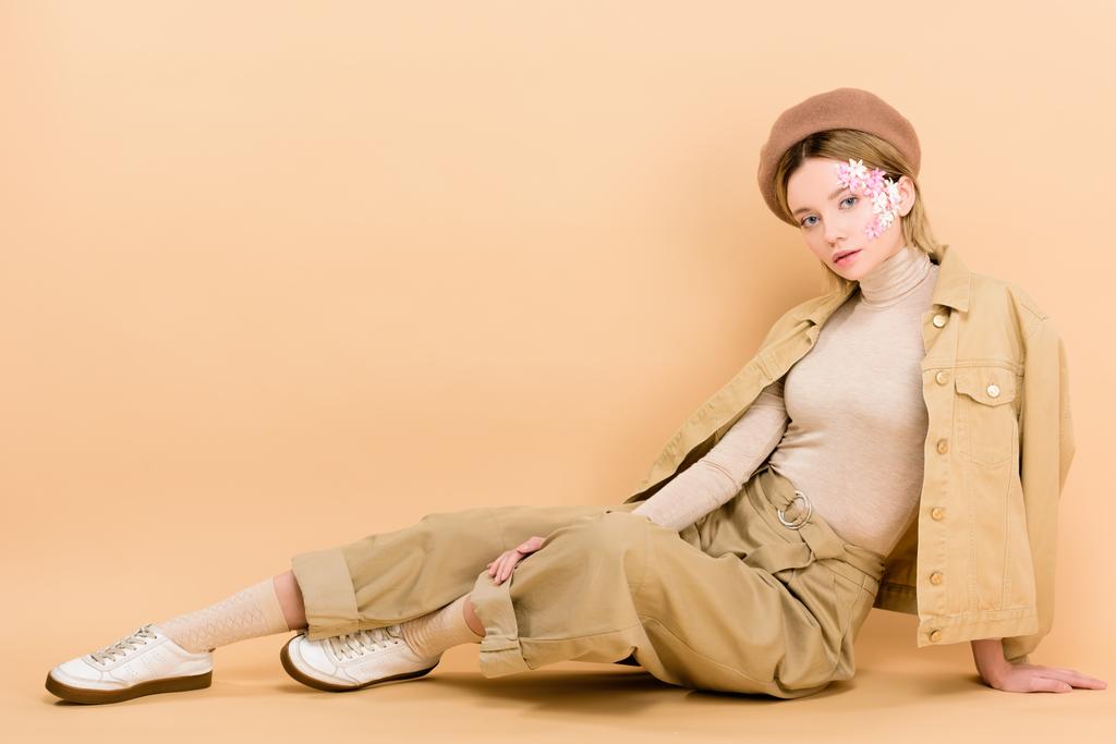 fille à la mode dans béret posant tout en étant assis sur le sol isolé sur beige
  - Photo, image