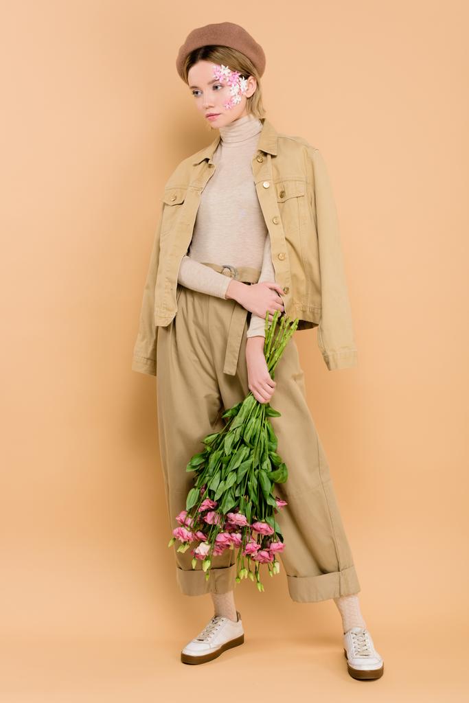 stilvolles Mädchen in Baskenmütze stehend mit Strauß isoliert auf beige  - Foto, Bild