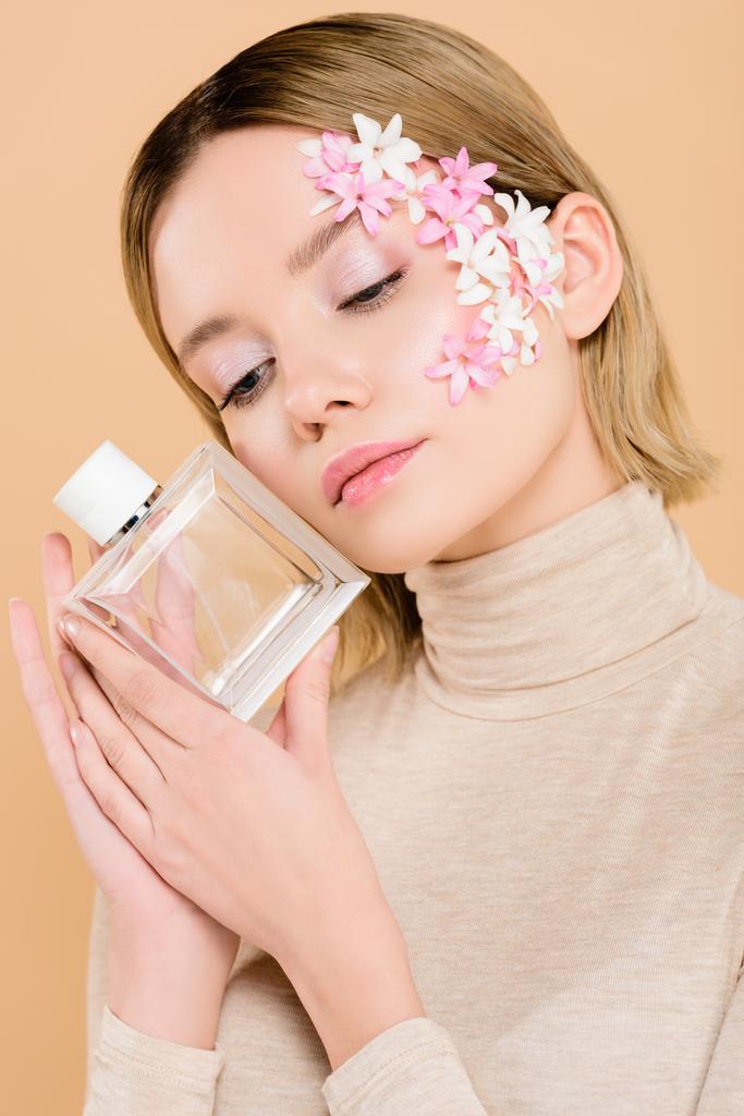 attraktive Frau mit Blumen im Gesicht, die eine Flasche Parfüm auf Beige hält - Foto, Bild