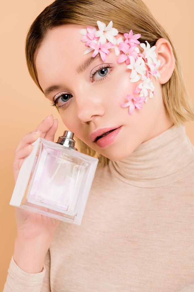 jolie femme avec des fleurs sur le visage tenant bouteille de parfum à la main isolé sur beige
 - Photo, image