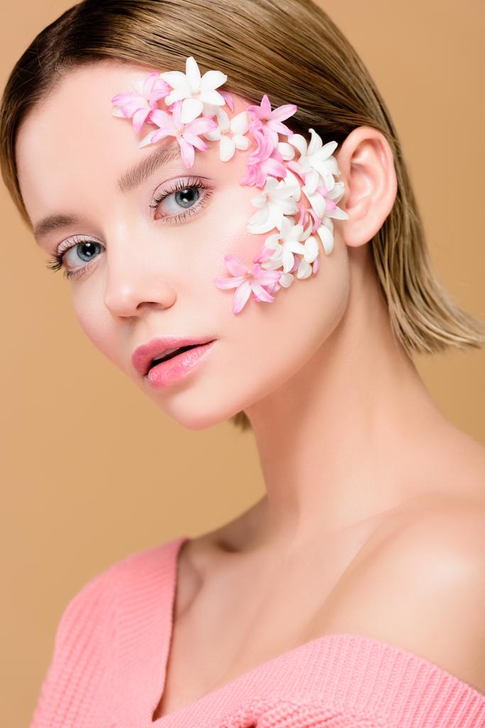 tendre femme avec des fleurs sur le visage regardant caméra isolé sur beige
 - Photo, image