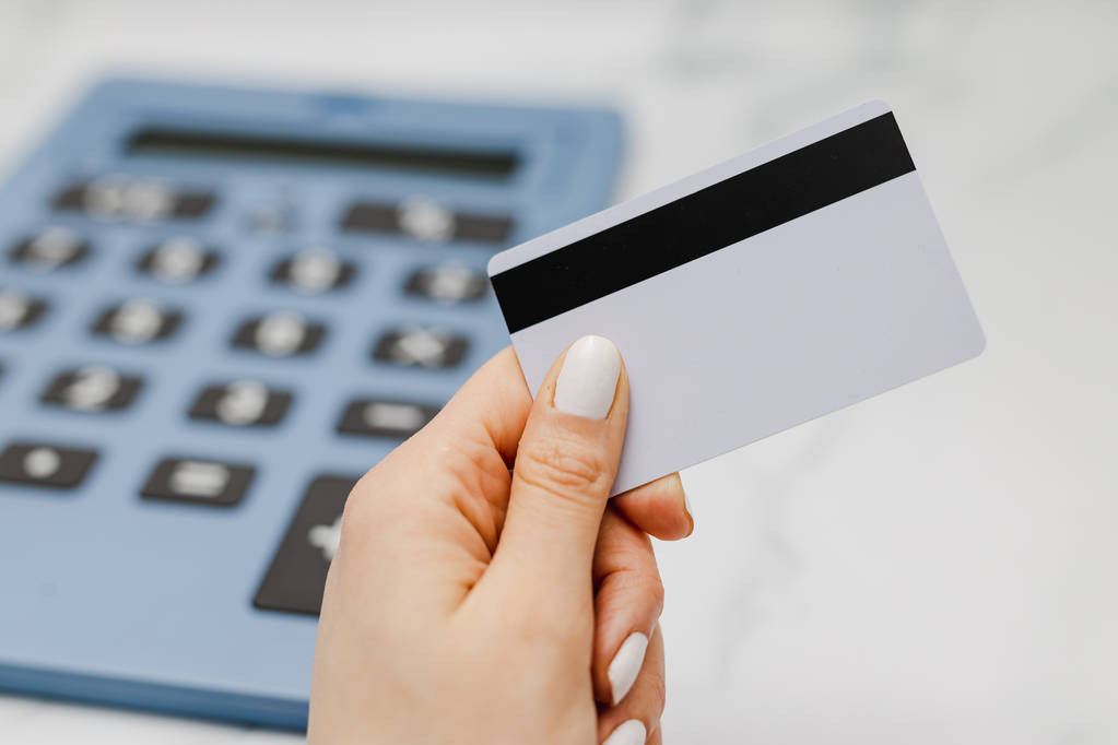 жіноча рука тримає платіжну картку перед величезним калькулятором, концепція торгового бюджету
 - Фото, зображення