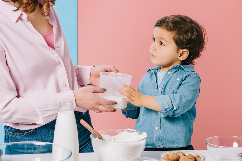 ładny chłopczyk z Mama, trzymając miarkę z mąki na tle bicolor na tle bicolor - Zdjęcie, obraz