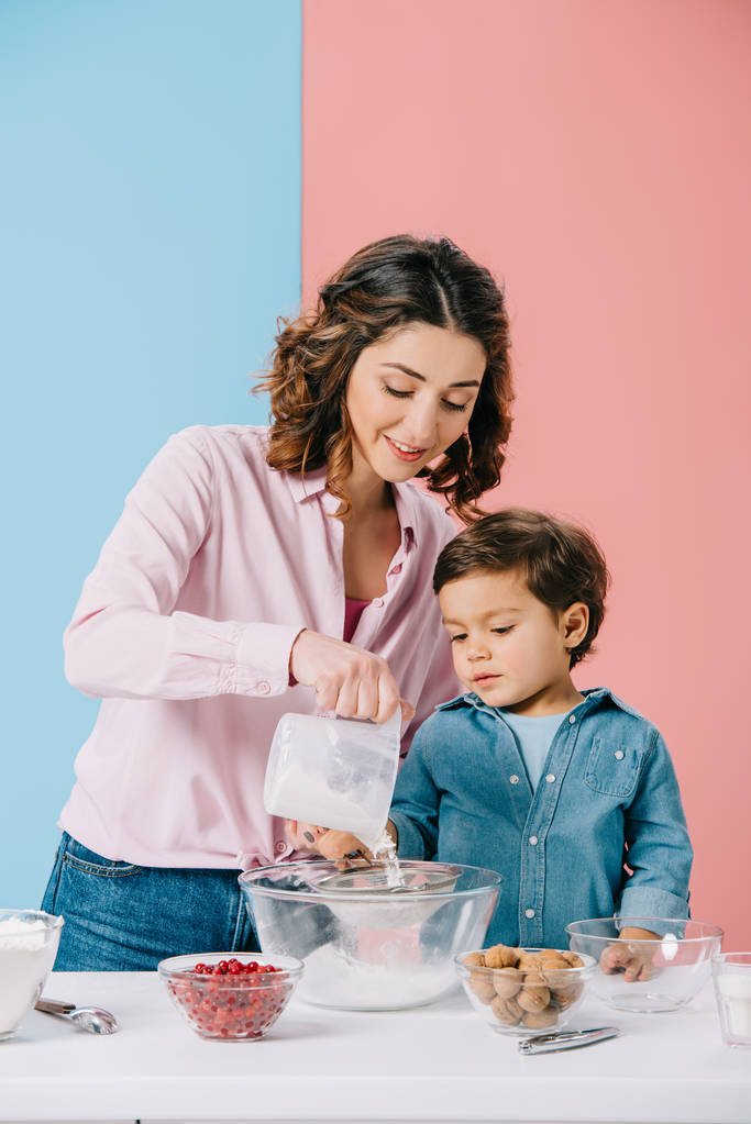 bonita mamá con lindo pequeño hijo tamizar harina para tazón juntos sobre fondo bicolor
  - Foto, imagen