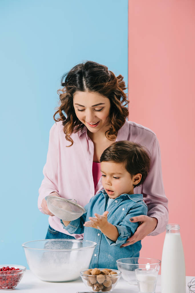 beautiful mother with cute little son cooking together on bicolor background - Photo, Image