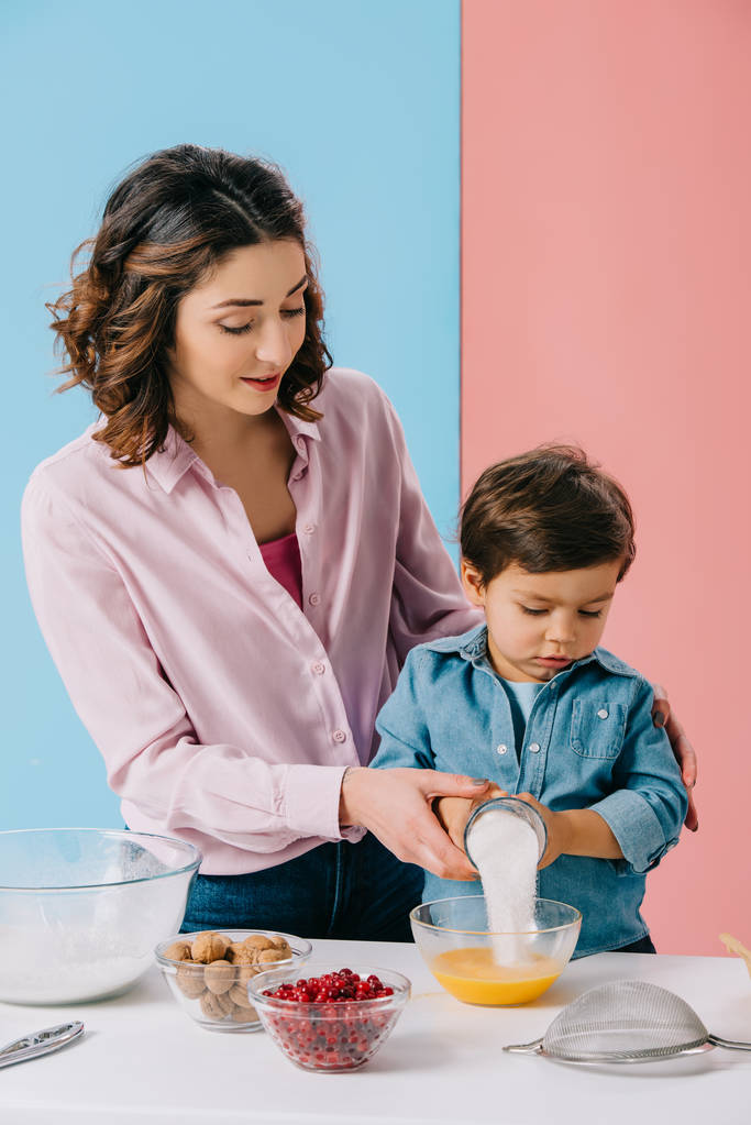 moeder helpen zoontje toevoegen van suiker aan de slagroom eieren op bicolor achtergrond - Foto, afbeelding