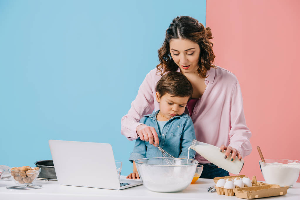 милый мальчик смотрит на дисплей ноутбука в то время как мать трещит грецкий орех на двухцветном фоне
 - Фото, изображение
