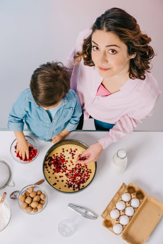 top view of mother and son adding cranberries to dough in baking form on light background - Photo, Image