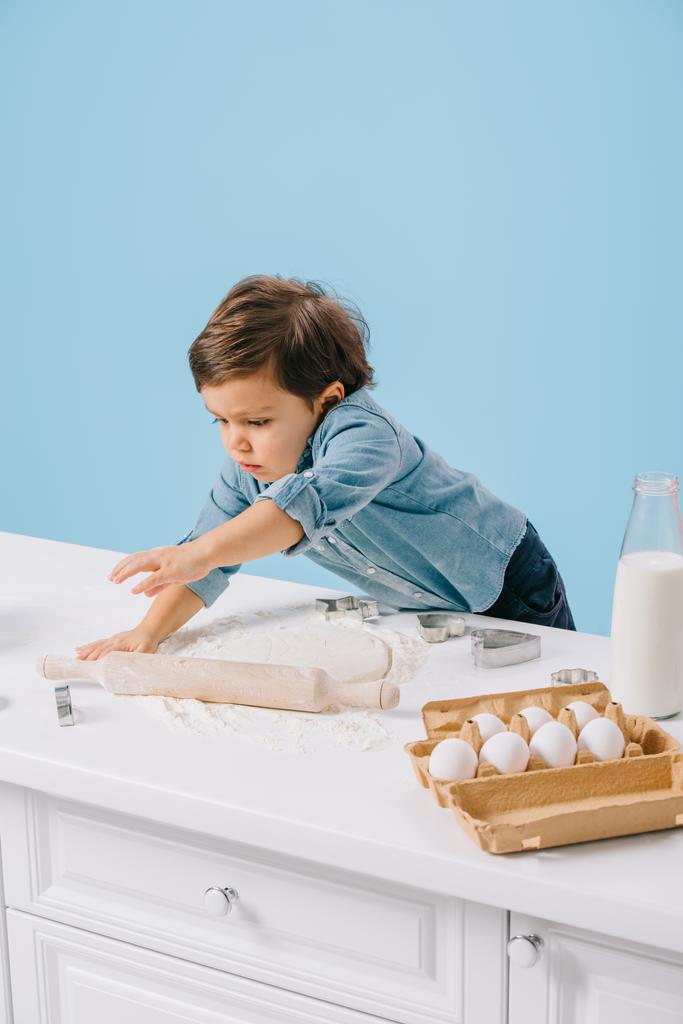 cute little boy rolling out dough with rolling pin isolated on blue  - Photo, Image
