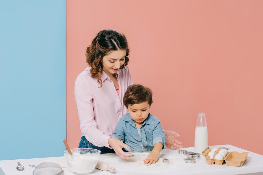 smiling mother with cute little son cooking pastry together on bicolor background  - Photo, Image