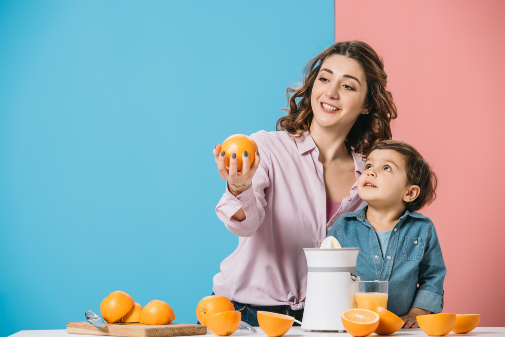 sorridente mãe mostrando todo laranja para bonito pequeno filho no fundo bicolor
  - Foto, Imagem