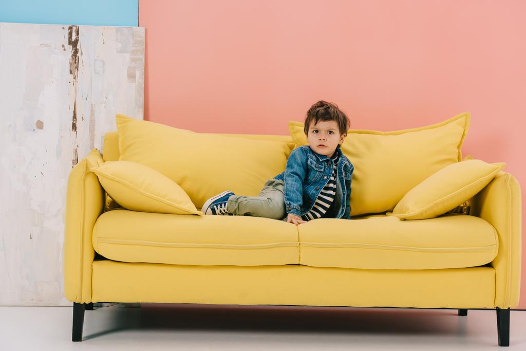 carino bambino in giacca blu e jeans verdi seduto sul divano giallo
 - Foto, immagini
