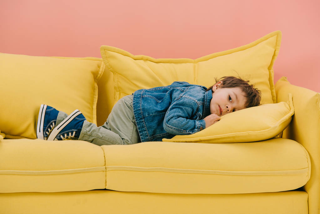 cute little boy in blue cotton jacket and green jeans laying on yellow sofa - Photo, Image