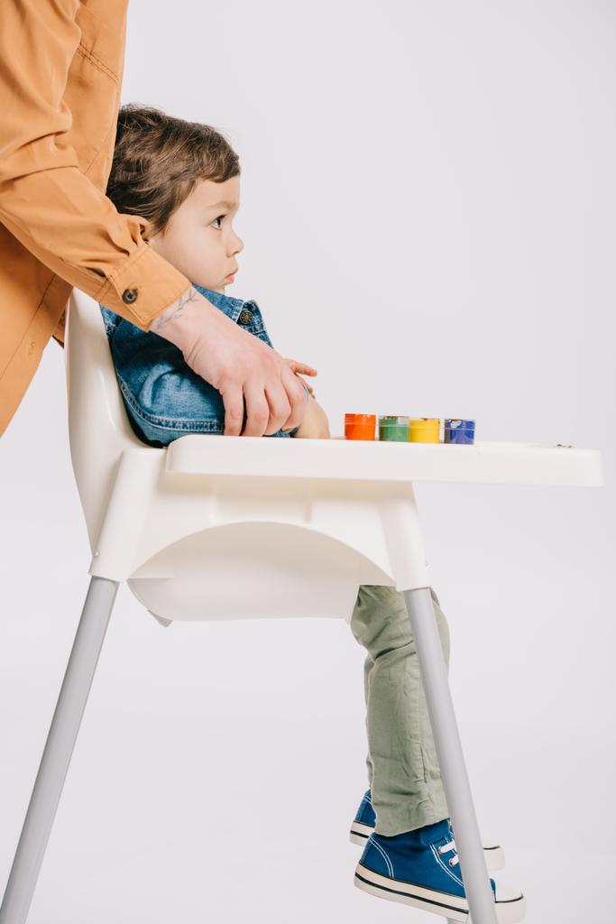 matka, objímala malý syn sedí na židličku s akvarely na stůl izolované na bílém - Fotografie, Obrázek