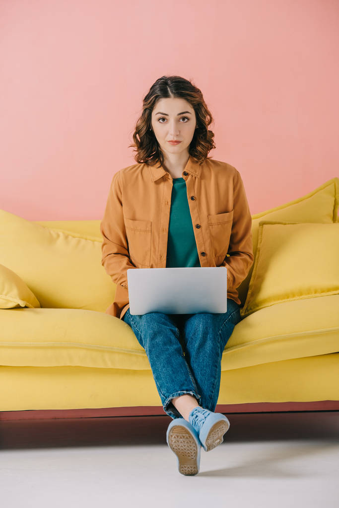 beautiful young woman sitting on yellow sofa and using laptop - Photo, Image