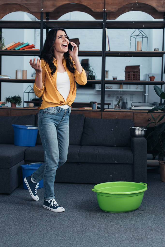 Chica estresada en camisa amarilla hablando por teléfono y mirando el techo con fugas
 - Foto, imagen