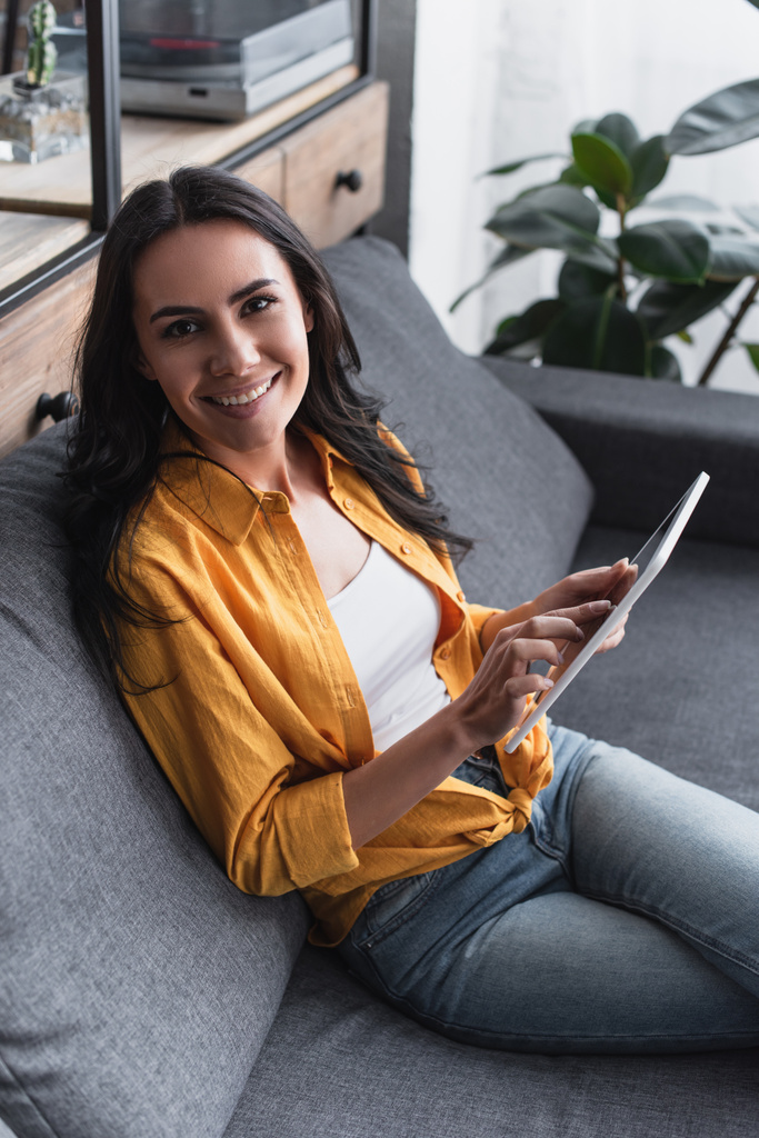 fröhliche Frau im gelben Hemd sitzt auf Sofa mit digitalem Tablet - Foto, Bild