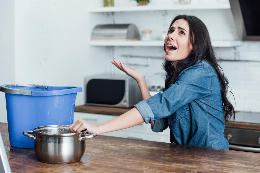 Mulher morena estressada lidando com danos causados pela água na cozinha
 - Foto, Imagem