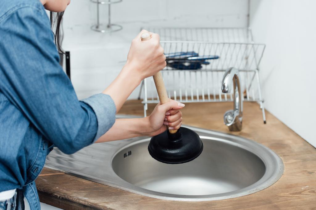 Partial view of woman in denim shirt using plunger in kitchen - Photo, Image