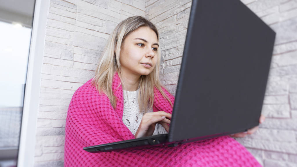 Hermosa mujer joven con un ordenador portátil y cuadros calientes sobre un fondo de ladrillo blanco
 - Foto, imagen