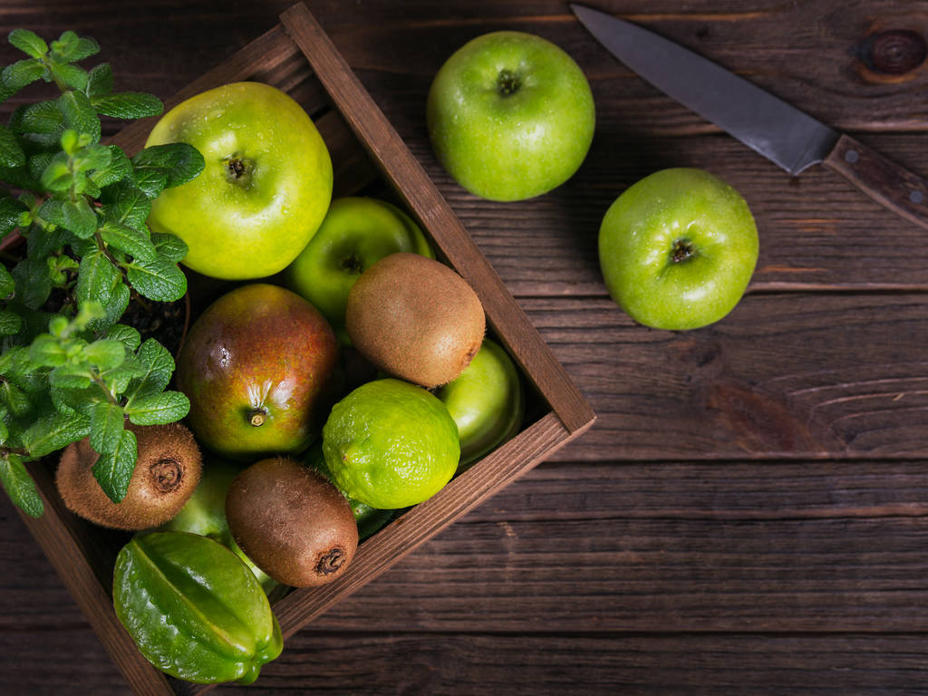 Fondo alimentario saludable. Concepto de comida saludable. Frutas verdes frescas en caja sobre fondo de madera oscura. Conjunto de frutas verdes para una dieta saludable y desintoxicación: manzana, lima, kiwi, carambola y menta. Puesta plana
 - Foto, Imagen