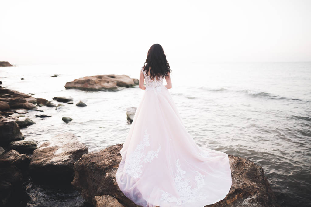 Красивая леди, невеста позирует в свадебном платье у моря на закате - Фото, изображение