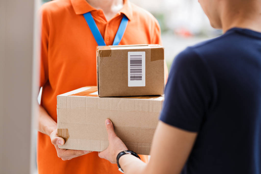 Eine Person in orangefarbenem T-Shirt und Namensschild liefert Pakete an einen Kunden aus. freundliche Arbeiter, qualitativ hochwertiger Lieferservice - Foto, Bild