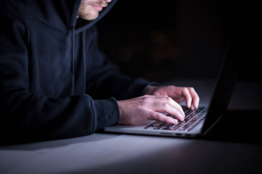 Joven hacker talentoso usando computadora portátil mientras trabaja en la oficina oscura con grandes luces de la ciudad en el fondo por la noche - Foto, imagen