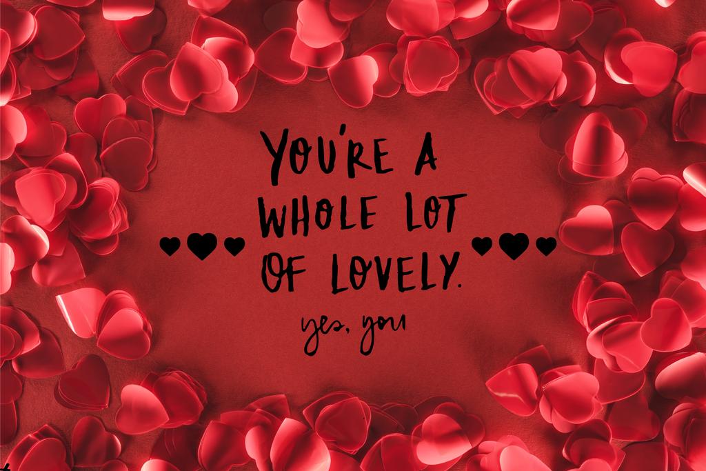 top view of decorative heart shaped petals on red background with "you are a whole lot of lovely, yes you" lettering, valentines day concept  - Photo, Image