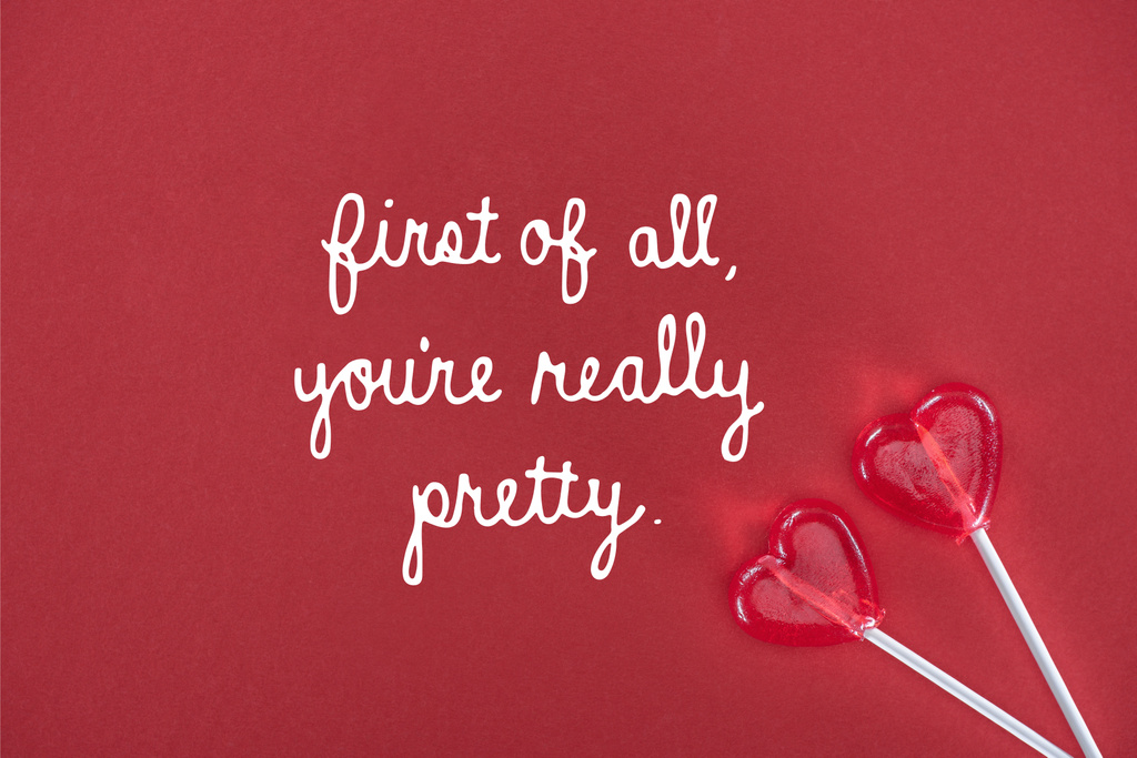 vista superior de dos piruletas en forma de corazón sobre fondo rojo con letras "en primer lugar, eres realmente bonita", concepto de día de San Valentín
  - Foto, Imagen