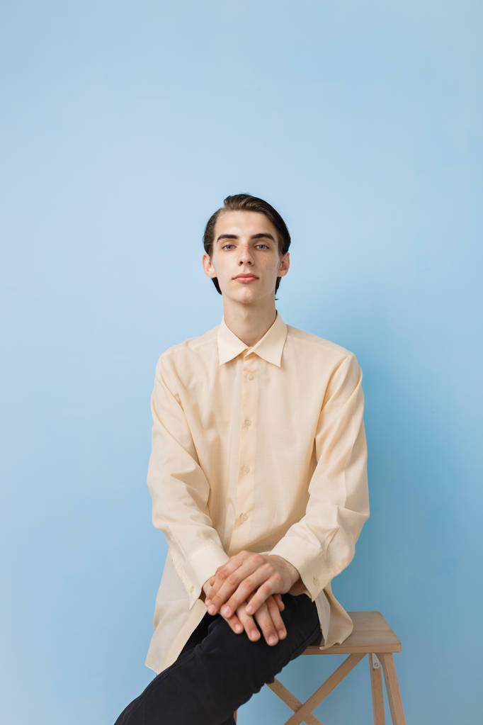 Красивый молодой худой темноволосый парень с голубыми глазами в жёлтой рубашке, позирующей над синей стеной.
 - Фото, изображение