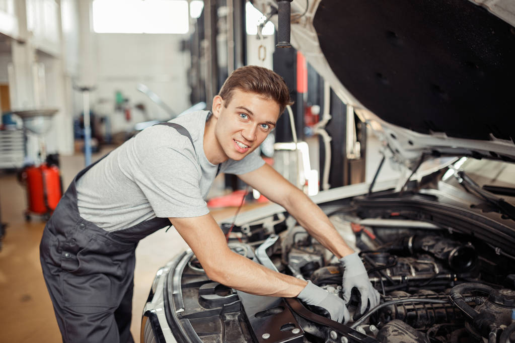 Молодой красивый мужчина проверяет двигатель машины на автосервисе
 - Фото, изображение