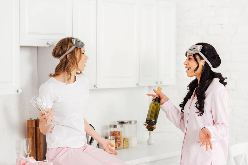 beautiful multicultural girls talking and celebrating with champagne during pajama party in kitchen - Photo, Image