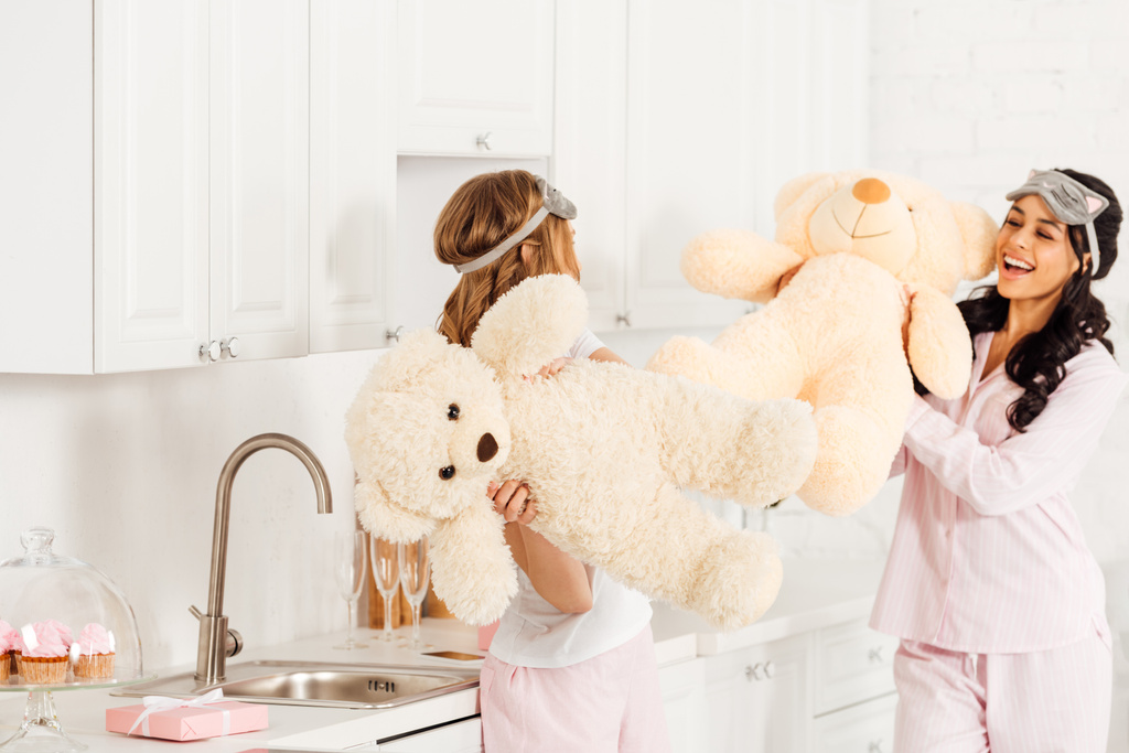 mooie multiculturele meisjes spelen met teddyberen tijdens pyjama party thuis - Foto, afbeelding