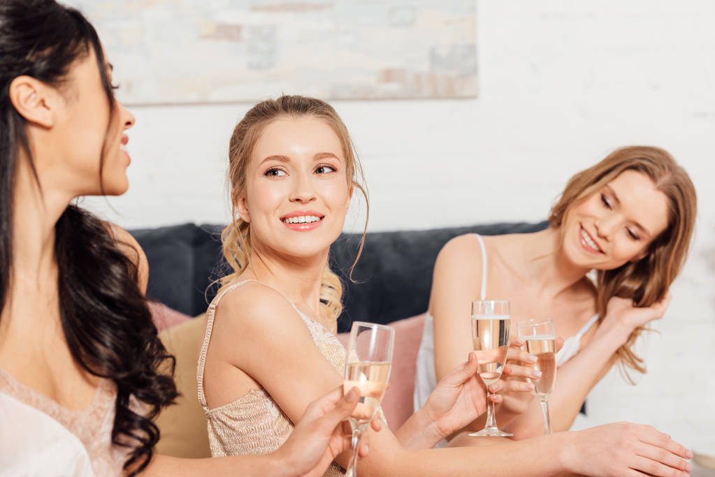 mooie lachende multiculturele meisjes in nachtkleding met champagneglazen tijdens pyjama party - Foto, afbeelding