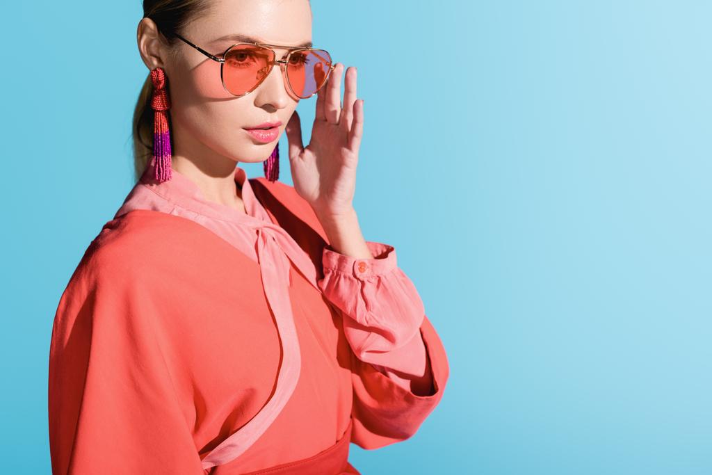 красива стильна дівчина в модному життєвому кораловому одязі і сонцезахисних окулярах позує ізольовано на синьому
 - Фото, зображення