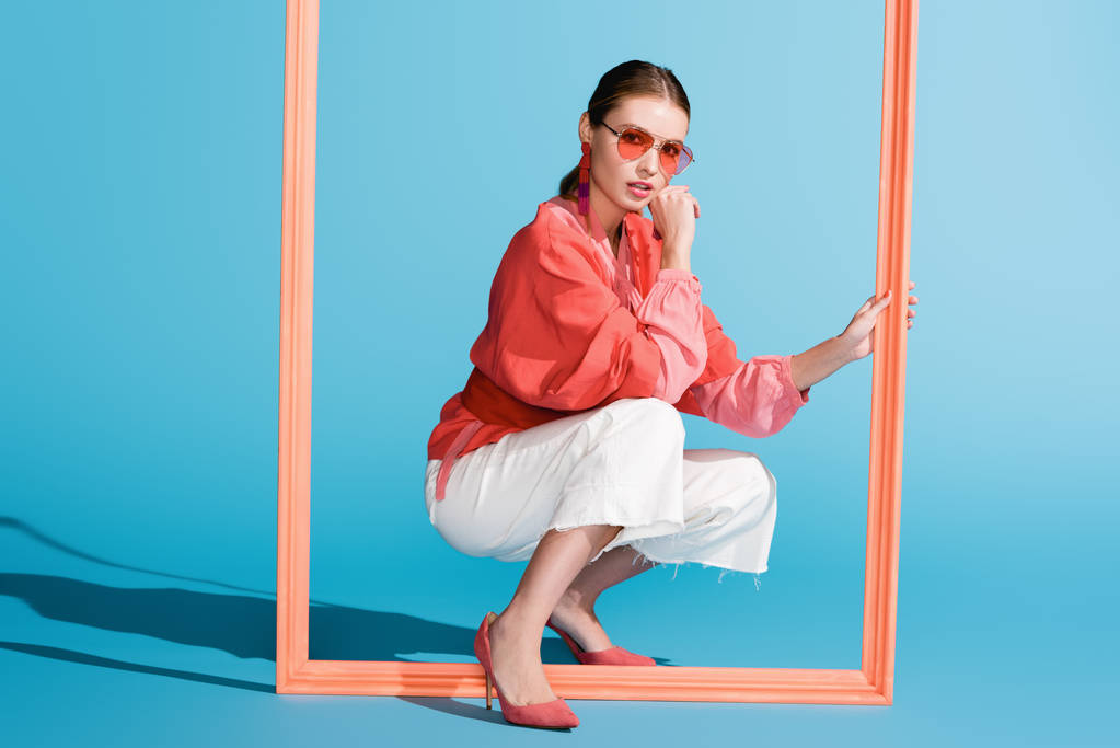 modelo con estilo en la ropa de coral vivo y gafas de sol posando con marco grande en azul
 - Foto, Imagen