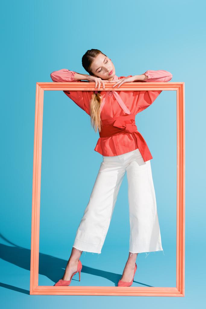 fashionable elegant woman in living coral clothing posing with big frame on blue - Photo, Image