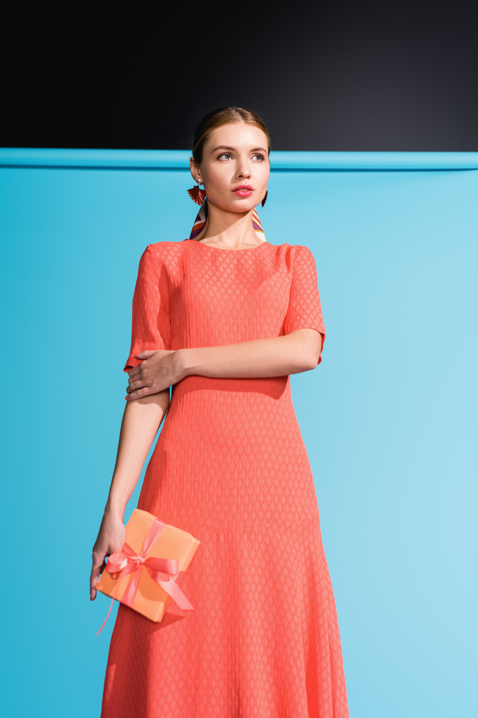 fashionable woman in living coral dress holding gift box on blue - Photo, Image