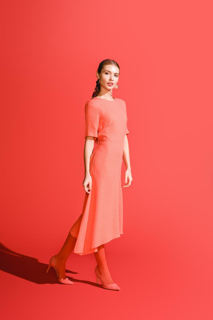 elegante stijlvolle meisje poseren in levende koraal jurk op rode achtergrond - Foto, afbeelding